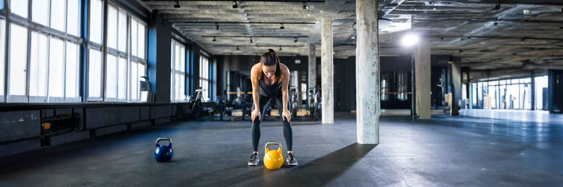 Woman with hands on knees in the gym with a kettlebell looking tired