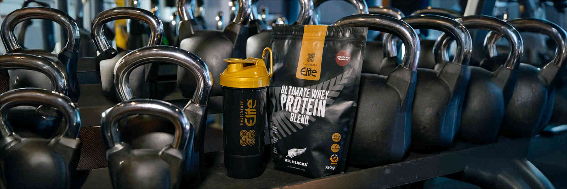 Healthspan Elite Whey Protein on a rack with kettle bells