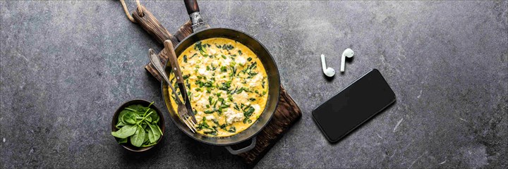 Egg and spinach omelette in a pan with phone and earbuds next to it